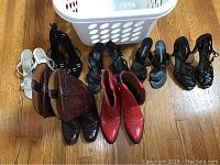 Image shows six pairs of women's shoes on wooden floor including brown embossed boots, red knee-high boots, black and silver high heel sandals.