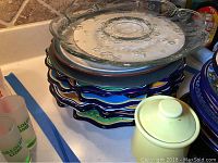 Stack of colorful Mexican artwork ceramic plates with 2 clear glass trays and yellow sugar holder on top