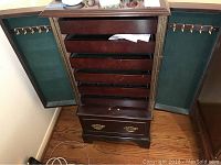 Jewelry cabinet open, showing six felt-lined drawers and green felt-lined doors with brass hooks for hanging necklaces.