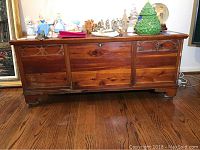 Front view of the solid wood cedar chest showing the wood grain, feet, and some wear on the surface. Chest is closed.