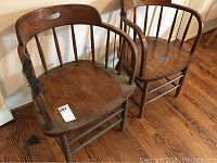 Two vintage wooden barrel chairs side by side on hardwood floor with some scratches and age wear visible.