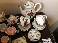 Miniature tea service set including teapots, sugar containers, and cups with saucers with floral patterns displayed on dark surface.