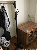 Full view of the black metal coat rack standing next to a laundry basket and wooden cabinet, showing overall height and design.