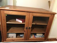 Rectangular wooden cabinet with glass doors and visible interior shelves with books and boxes.