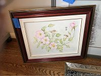 Framed print with pink flowers and green leaves in a wood frame.