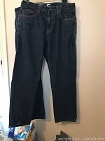 Full length view of one pair of blue denim jeans hung on hanger showing cut and wash
