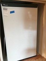 Front view of Whirlpool white mini fridge showing exterior door with Whirlpool logo and blue tape with size info.