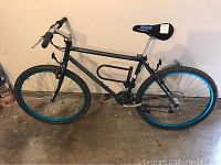 Full side view of the men's bicycle showing the blue rims, scratched dark frame, torn seat, and flat tires.