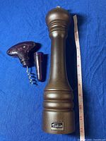 Full view of the 12-inch wooden Trudeau pepper mill and wine opener on blue background with measuring tape.