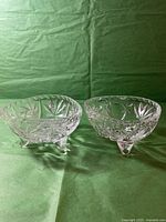 Front view of two clear cut crystal vases showing detailed cut patterns and three small feet on each.