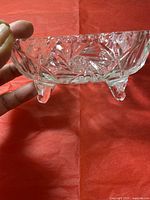 Close up view of square-shaped crystal vase showing three small curved legs and detailed cut starburst and geometric patterns.