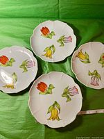 Four white plates with scalloped edges, each featuring three tulips in red, yellow, and purple, placed on a green background.