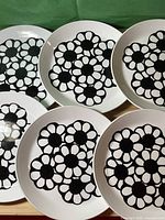 Set of six 6-inch white plates with bold black floral design on top side.