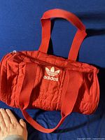 Front view of red Adidas sports/gym bag laid flat with Adidas logo on front and double handles.