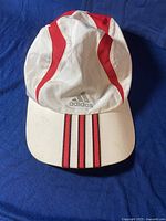 Top/front view of the Adidas white and red baseball hat showing the curved brim with three red stripes and front Adidas logo.