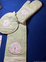 Entire kitchen set arranged on blue background showing oven mitt, pot holder, and kitchen towel with bunny face embroidery.