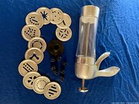 Image showing the decorating tool with clear main body and metallic top, large collection of decorating discs and black plastic attachments arranged on blue fabric