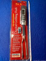 Photo of the digital grilling fork in original red and black packaging with product details and logo visible.