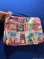 Photo showing front side of large fabric travel cosmetic bag with colorful patchwork prints featuring various artistic and travel-themed images. Tag attached at top corner.