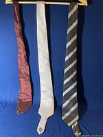 Three men’s ties hanging on a hanger on a dark blue background, showing colors and patterns of each tie.