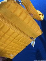 Detailed view of top zipper closure and quilted yellow fabric of the bag.