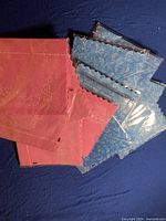 Blue and pink decorative paper napkins with floral patterns and scalloped edges, laid out on dark blue fabric background.