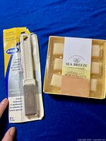 Dr. Scholl's callus filer in original packaging alongside an open box of Sea Breeze exfoliating cubes.