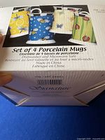 Box showing set of 4 porcelain mugs with images of bees, butterflies, and ladybugs and details about dishwasher and microwave safety.