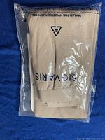 Photo of sealed beige Sigvaris compression stockings in transparent plastic packaging on blue fabric background, showing the stockings folded with brand name partially visible.