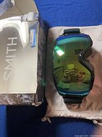 Smith Grom goggles with reflective ChromaPop lens, placed next to original box and beige pouch.