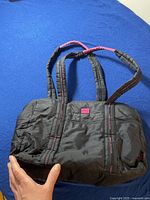 Black Tommy Hilfiger shoulder bag held on a blue surface, showing overall shape and design with pink strap accents.