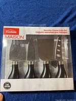 Front view of box showing four cheese tools with black handles and stainless steel blades