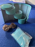 Turquoise folding jewelry box open with multiple round compartments, fabric hair clip, and packaged turquoise folding bag.