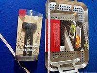 Wine corkscrew in original packaging next to grill pans on blue cloth background with measuring tape