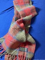 Full view of the men's wool scarf on blue background showing red and green plaid pattern and fringed ends.