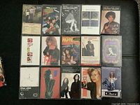 Photo of 15 rock cassette tapes arranged on black surface, various artists and albums visible including Elton John, Cher, Whitney Houston, Pulp Fiction soundtrack and others.
