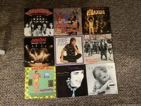 Photo shows nine 45 RPM vinyl records arranged in a 3x3 grid, featuring bands Judas Priest, Saxon, and others