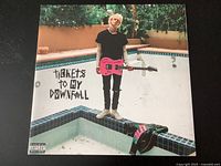 Front of the album cover showing Machine Gun Kelly with a pink guitar standing in an empty pool with the album title 'Tickets to My Downfall'.