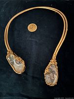 Full view of collar choker laid flat on dark fabric with quarter for scale