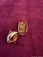 Pair of amber earrings laid on red fabric background, showing polished oval amber stones in metal setting.