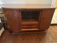 Front view of the walnut buffet showing curved sides, glass top, central glass sliding cabinet, and two drawers below.