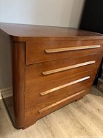 Side and front angle view showing the walnut wood dresser with four drawers and horizontal wooden handles in Art Deco style.