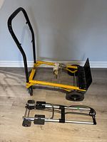 Side view of the adjustable medium duty dolly with yellow metal frame and black handle, showing the medium duty base and small folding luggage dolly folded nearby.