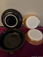 Top and bottom view of two black Fiestaware shallow bowls and two peach depression glass bowls showing the muted logo and overall condition.