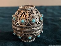Closed filigree sterling silver sphere with turquoise accents on dark fabric background