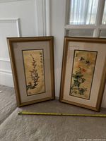 Two Japanese gold foil framed prints leaning against a wall on carpet with measuring tape showing their approximate height.