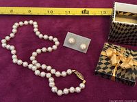 Knotted imitation pearl choker necklace and matching imitation pearl stud earrings displayed next to measuring tape with decorative box included.