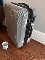 Exterior front side of the suitcase with black and white houndstooth pattern, standing upright, showing side handle and wheel.