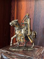 Side angle view of pewter and brass knight figurine showing intricate details of horse and knight on glass pedestal.