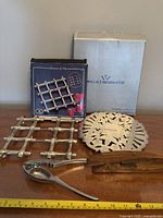 Photo of two silver-plated trivets, boxes behind them showing brand Wallace Silversmiths and another brand for one trivet.